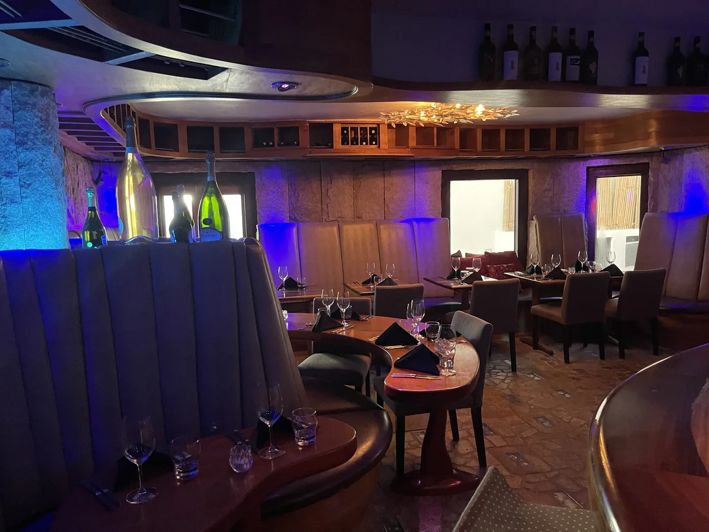 Niche Restaurant interior with mahogany wine wall and warm chandelier under violet light